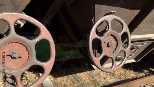 Close-up footage of rusty metal wheels on an old railway wagon standing on tracks in sunlight. The video captures aged industrial machinery, textured metal surfaces
