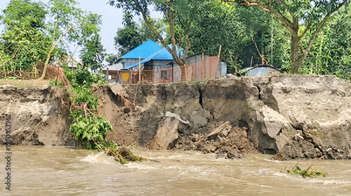 Eroded riverbank with a small village and blue-roofed house in the background erosion landslide