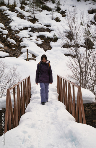 A young girl hiking with a backpack, walking across a snow-covered bridge. 