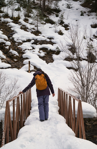 A young girl hiking with a backpack, walking across a snow-covered bridge. 