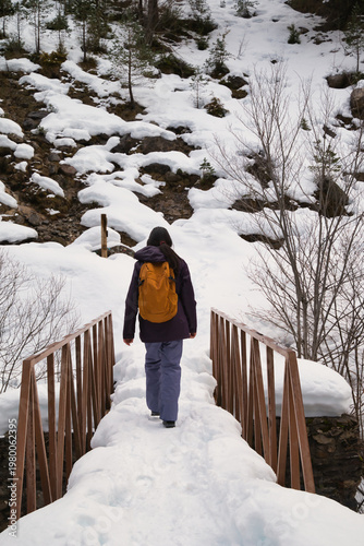 A young girl hiking with a backpack, walking across a snow-covered bridge. 