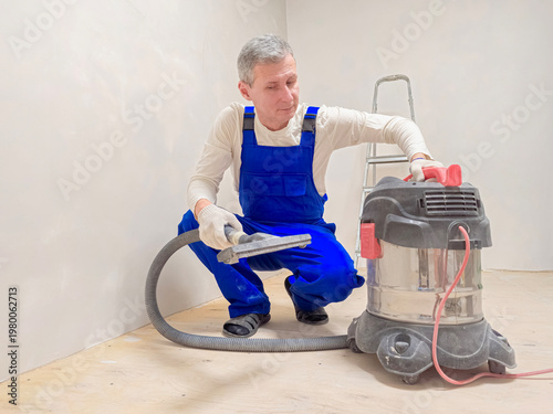 Man cleans floor with vacuum cleaner.