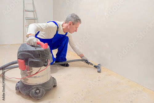Man cleans floor with vacuum cleaner.