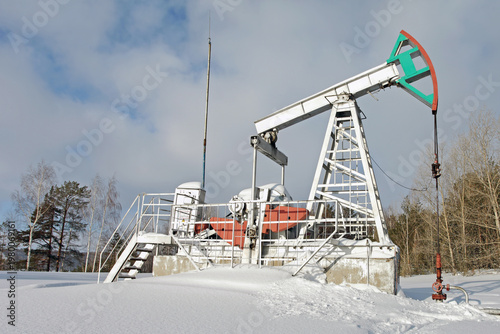 Oil pumpjack in snowy landscape, industrial equipment against winter forest backdrop, cold climate oil extraction
