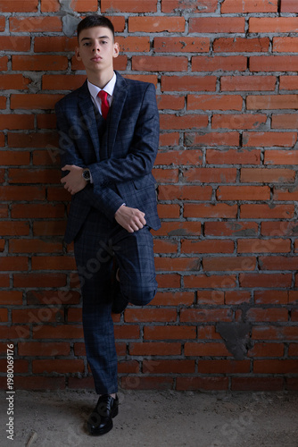 Young man in formal suit leaning against red brick wall