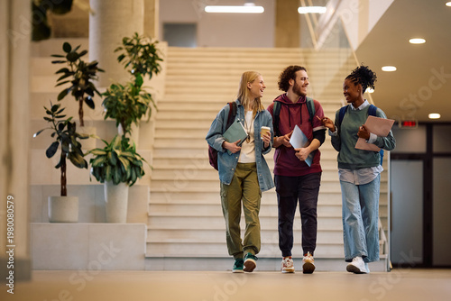 Happy diverse students talking while walking through university hallway.
