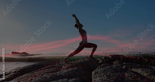 Woman practicing yoga stepping into deep lunge on rocky shore, stabilizing balance under pink light