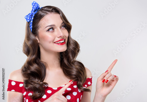 A Pin Up young smiling woman in a retro outfit points to the side, showcasing an invisible Presenting your product .Beautiful vintage girl with curly hair  .Expressive facial expressions