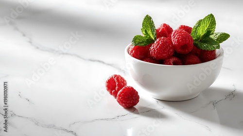 A bowl of fresh raspberries with mint leaves on a marble countertop
