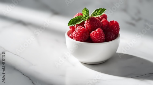 A bowl of fresh raspberries with mint leaves on a marble surface
