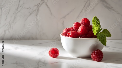 A white bowl filled with fresh raspberries and mint leaves on a marble countertop