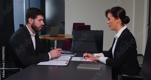 Focused serious woman, young businessman planning agreement with skilled lawyer, concentrated financial advisor showing paper contract document to male client at meeting in office, developing idea