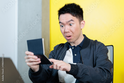 Принти на полотні An Asian male student stares wide-eyed in disbelief while pointing at his passport, ideal for expired travel document, visa complication, or international student emergency concepts