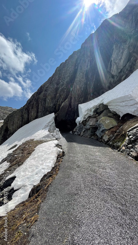 Mountain Road Leading into a Dark Tunnel with Snow and Bright Sun