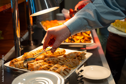 Wallpaper Mural Hand using tongs to serve grilled chicken rolls with sauce at a hot hotel buffet Torontodigital.ca