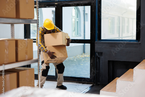 Canvastavla Delivery service african american loader carrying heave cardboard boxes and standing in warehouse office doors