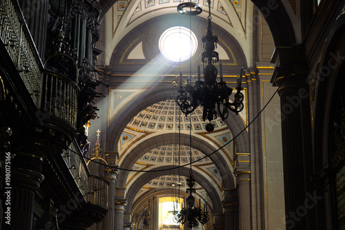 Dramatic divine sunbeam piercing through dome illuminating ornate interior of Cathedral with hanging chandeliers and gilded vaults creating spiritual atmosphere in Puebla, Mexico