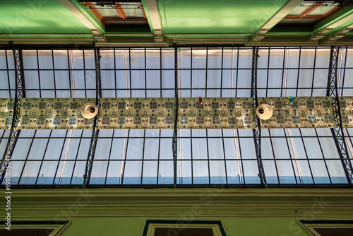 Detailed low angle view of ornate glass and iron ceiling with traditional Talavera tile band and hanging lamps inside historic passage in Puebla, Mexico