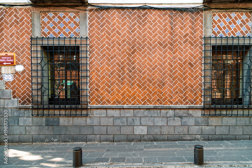 Historic facade covered in traditional Talavera tiles arranged in herringbone pattern with ornate wrought iron windows and street sign on Juan de Palafox y Mendoza avenue in Puebla, Mexico