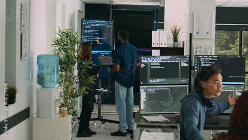 Fotografie Diverse team of system developers analyzing code on big tv screen, checking errors in artificial intelligence project
