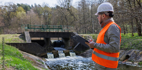 Fotografie Environmental engineer inspecting a river dam and water level control system for ecological monitoring