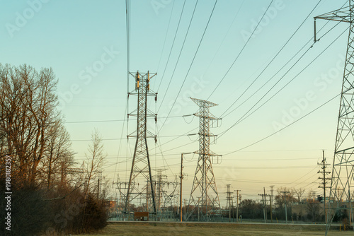 A horizontal shot of multiple transmission towers and power lines silhouetted against a vibrant sunset sky, symbolizing the vital role of sustainable energy in modern infrastructure