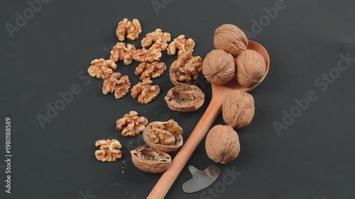 Top-down rotating macro of whole walnuts in shell and shelled kernels on a rustic wooden spoon. Black background. High-quality natural food concept.