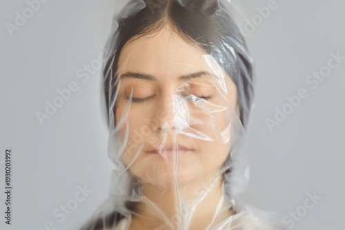 Photography Closeup portrait of a young woman with closed eyes wearing plastic bag on her head isolated on gray background as a protest against the use of plastic in the world