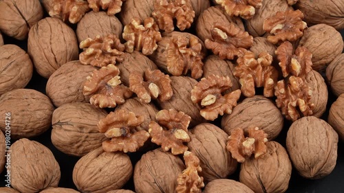 Top-down texture of shelled walnut kernels placed on top of raw whole walnuts in shells. Premium organic food background for nutrition projects.