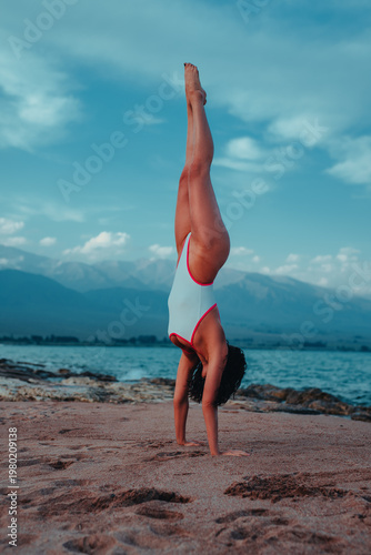 Woman doing handstand on beach with mountains