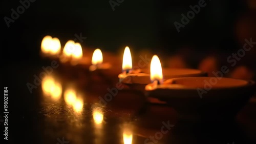Row of lit oil lamps casting warm glow and reflections in darkness.
