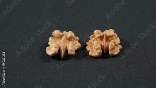 Close-up macro of two shelled walnut halves rotating on a black background. Premium minimalist organic food concept emphasizing brain-like shapes.