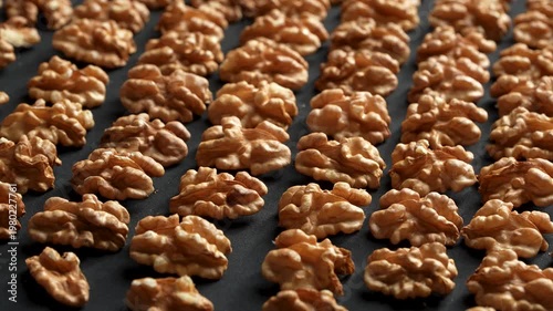 Neatly arranged rows of shelled walnut kernels rotating on a black background. Premium geometric organic food texture.