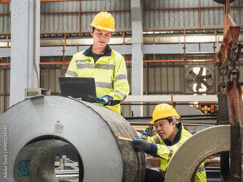 Two professional engineer safety vest hard hat collaborating in factory use laptop measuring tape inspect steel coil representing industrial teamwork quality control manufacturing excellence warehouse