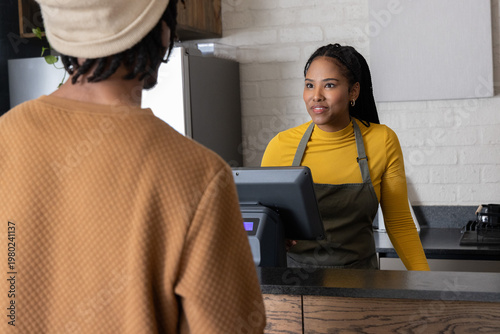 African American cashier and customer paying at cafe register, yellow top and apron, copy space