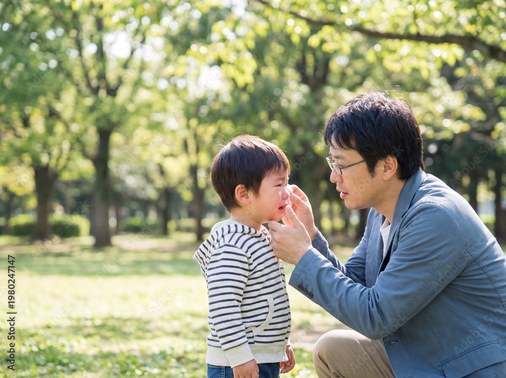 Fototapeta premium Caring Japanese Father Comforting Crying Toddler Son in Park