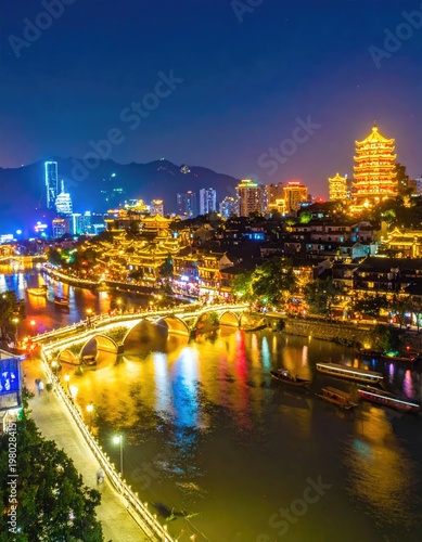 A vibrant nighttime cityscape showcases a historic pagoda and modern skyscrapers along a winding river, illuminated by colorful lights and framed by distant mountains.
