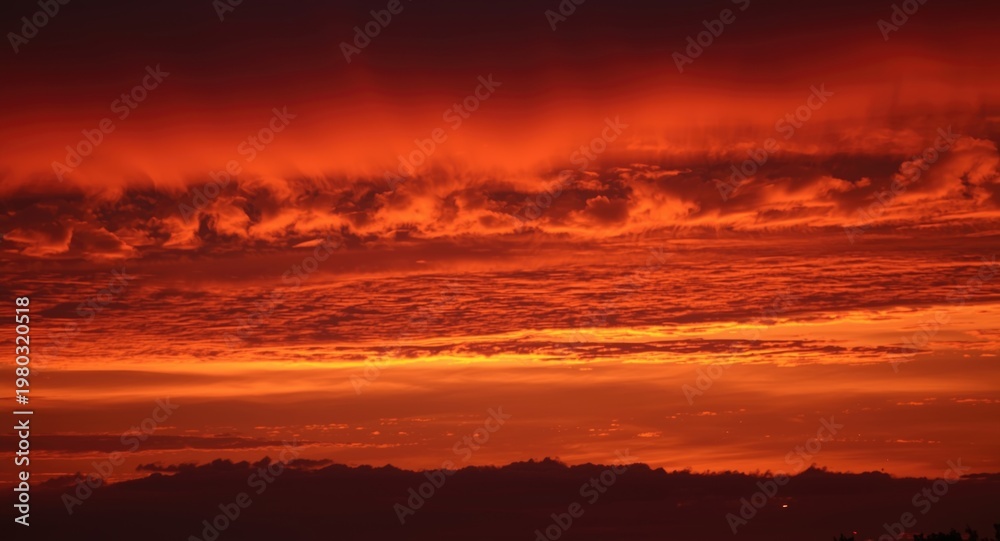 Fototapeta premium Vivid crimson and tangerine sunset sky casting shadows on clouds