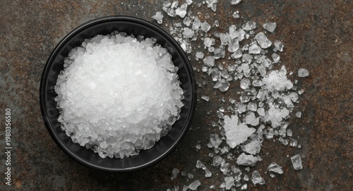 Top view of white citric acid crystals in a dark bowl on a textured surface showcasing natural granule patterns