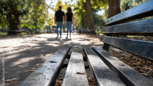 A scenic view of a park bench with a couple walking away in the background. The path ahead invites exploration, while the bench offers a place to rest and observe the beauty around