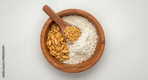 Top view of golden wheat grains and flour in a rustic wooden bowl with a spoon on white background