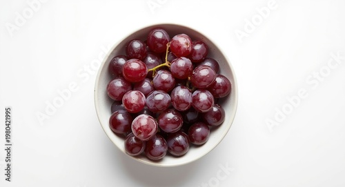 Glossy grapes presented inside a bowl on a plain bright white surface