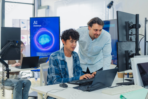 Caucasian mentor pointing at laptop screen while coaching young programmer in modern tech office, perfectly capturing teamwork, IT training, software development, and knowledge transfer.