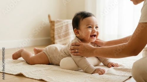 A baby lays on their stomach on a mat with a parent nearby, both enjoying playtime together