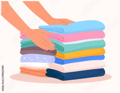 A pair of hands neatly folding and stacking a tall pile of freshly laundered, colorful towels and clothes.