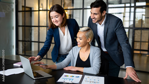 Business team collaborating on laptop in modern office setting with papers and charts