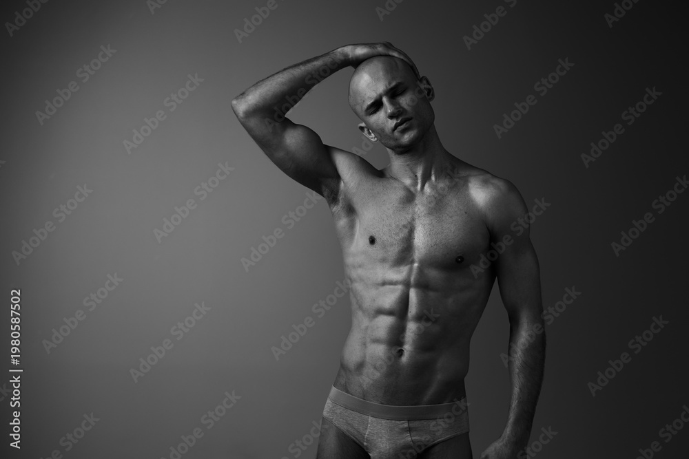 Fototapeta premium Black and white portrait of a man posing confidently, showcasing his toned physique and captivating expression. A striking image that emphasizes strength and elegance.