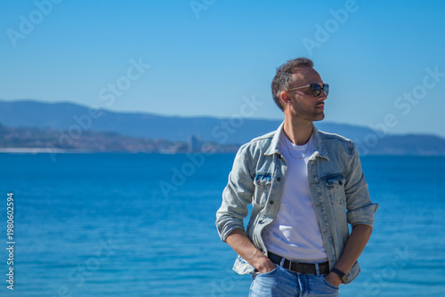 Foto A young man in a denim jacket and glasses walking along the coast