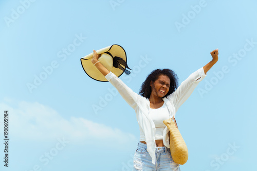 Happy African American woman raising arms on beach with sky background