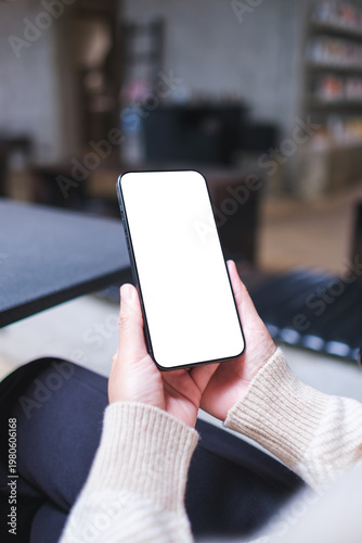 Vertical mockup image of a woman holding and using mobile phone with blank desktop screen